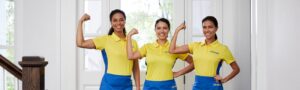 Photo shows three women in blue pants and yellow shirts doing fistpumps to show their strength. The shirts have The Maids logo on them.