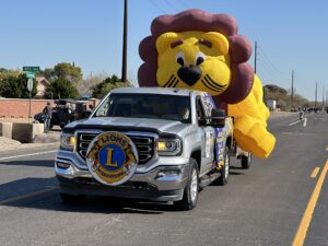 A silver truck is facing the camera with the Lions Club logo on the front bumper and massive, inflated Lion on the back of the truck.