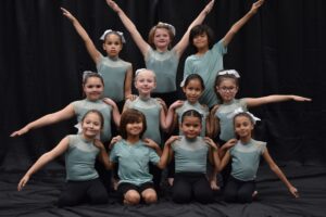 Photo shows a group of young dancers posing in green leotards with their arms out stretched.