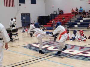 Laveen Karate photo shows two people wearing red belts sparring in a gynamsium as part of a karate tournament.