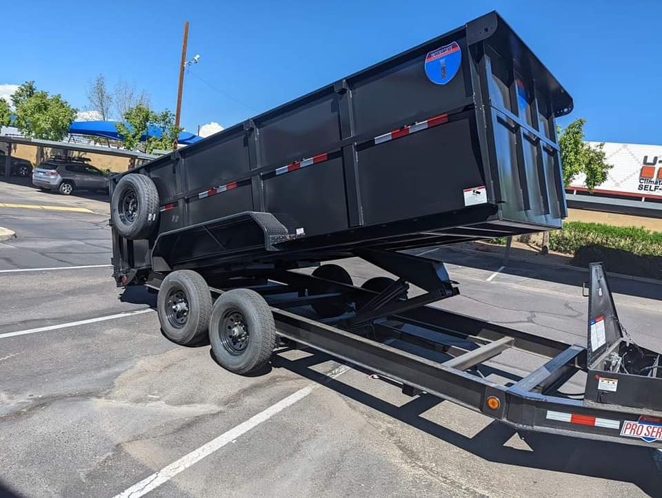 Photo shows a black dumpster on a trailer getting ready to be unloaded for MuscleMan Dumpster Rentals.