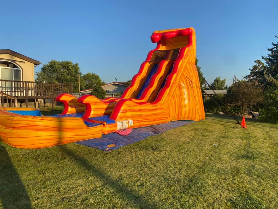 Photo shows a large orange inflatable dual slide and obstalce course in a large field.